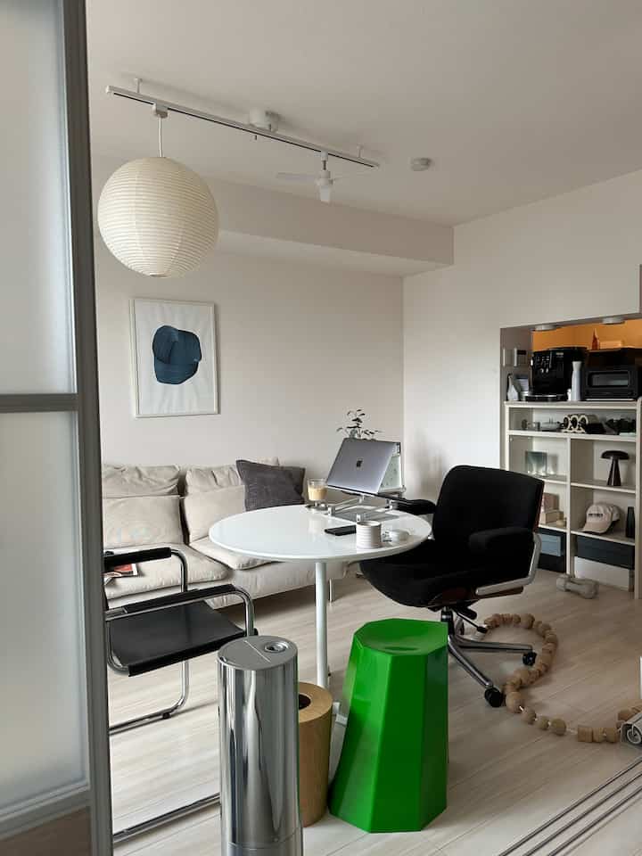 明るいホワイトと木目調の調和が取れたリビング兼ホームオフィス空間、モダンな家具と緑のスツールが配置された雰囲気のあるインテリア