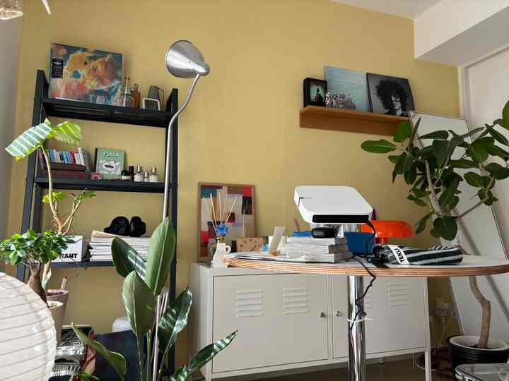 柔らかな黄色い壁と複数の植物がある一人暮らし向けのリビング、中央の円形テーブルにプロジェクターが置かれた雰囲気のあるインテリア