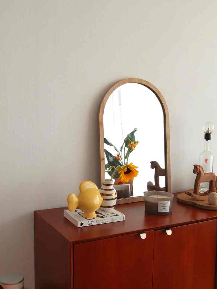 柔らかなブラウンとナチュラルトーンのリビング用サイドボードにアーチ型の鏡と花瓶、キャンドルが置かれたミニマルな空間