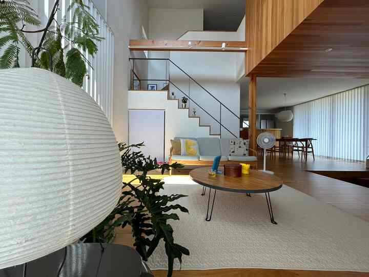 A white and brown living room featuring modern wooden furniture and a large pendant light, creating a natural and spacious atmosphere