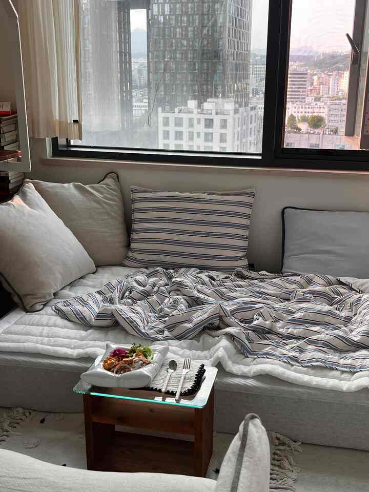 White and gray toned studio living room featuring a large window, sofa, and small table creating a cozy atmosphere