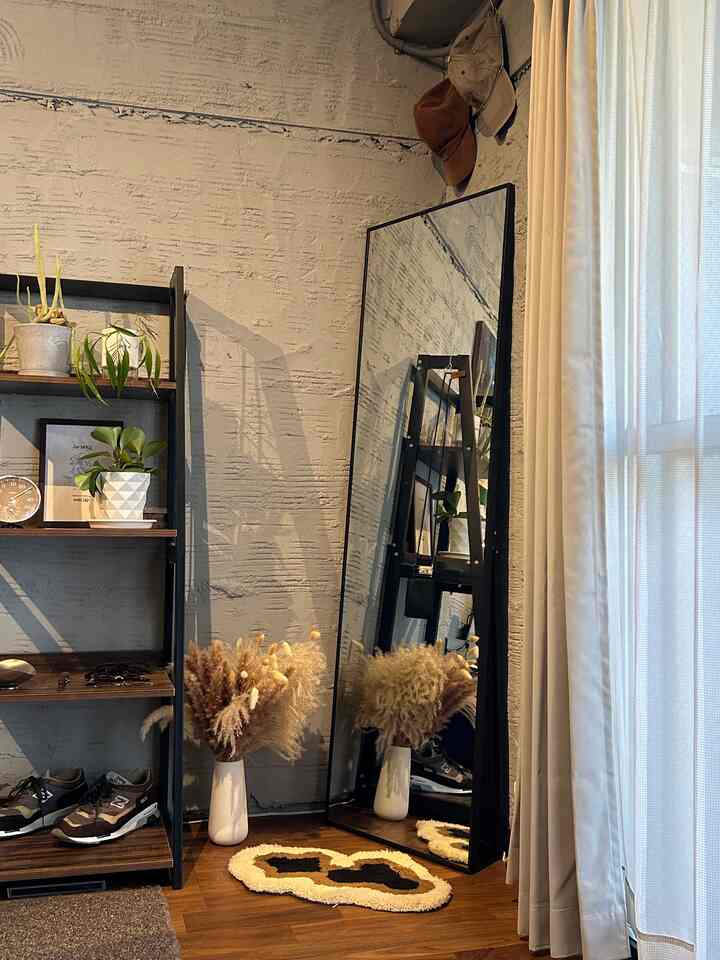 Natural toned living room corner featuring an open rack, a large full-length mirror, and a plush rug creating a cozy atmosphere