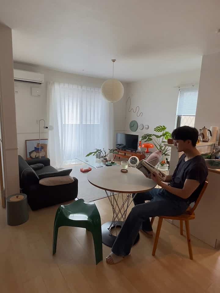 Bright white small living room and kitchen featuring round dining table, Mid-Century Modern furniture, and a person reading, cozy interior