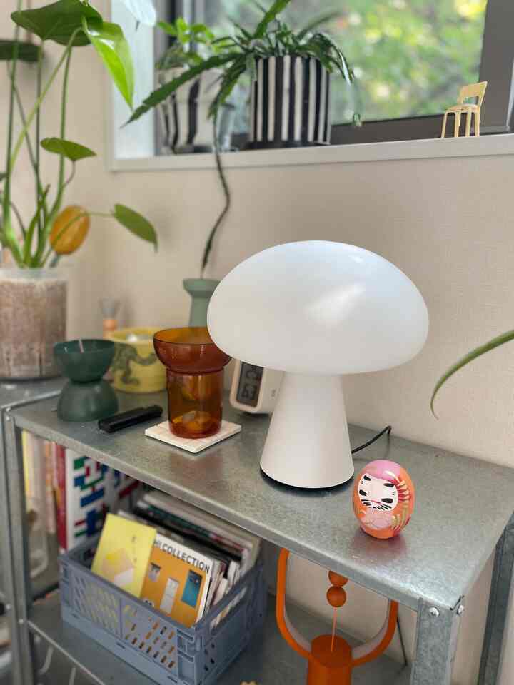 ナチュラルカラーとアンバー色調が調和する1Kの部屋、棚の上に白いキノコ型のテーブルランプとかわいいだるまのオブジェが配置された温かみのある空間