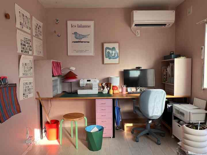 暖かいピンク色の壁と木製のデスクがあるホームオフィス空間で、ピンクのチェストやスツールが配置された雰囲気のあるインテリア
