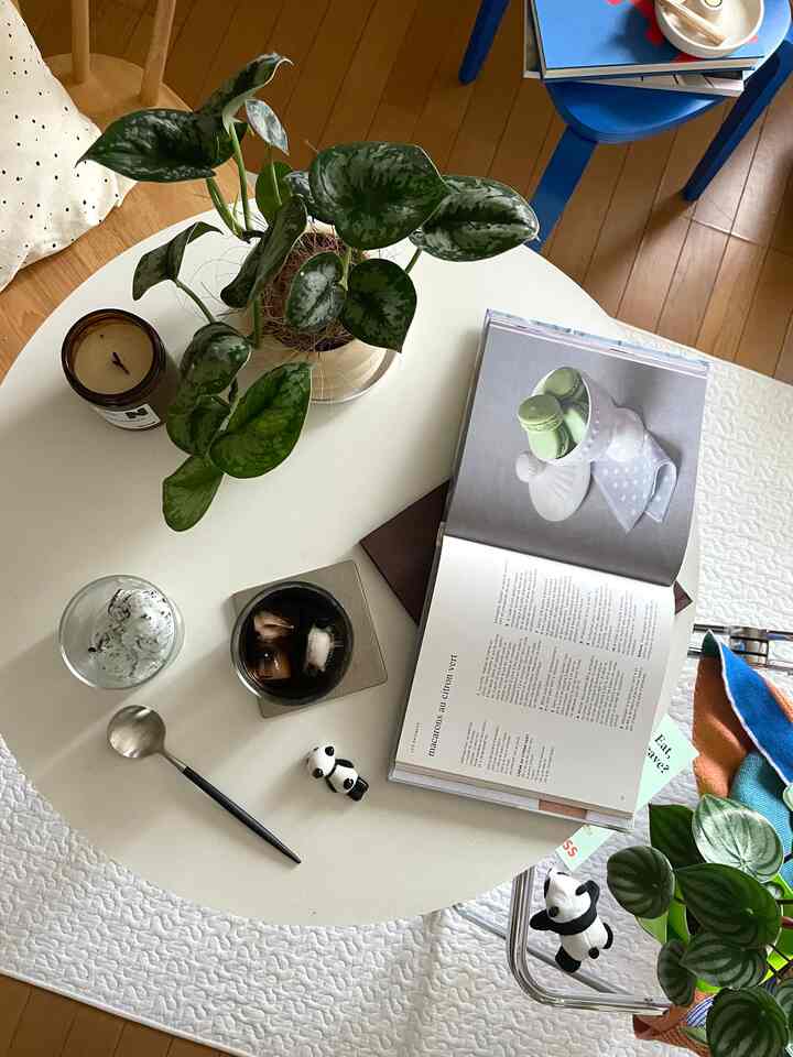 白いラウンドテーブルの上に植物とアイスドリンク、本が置かれたシンプルなおうちカフェの雰囲気あるインテリア