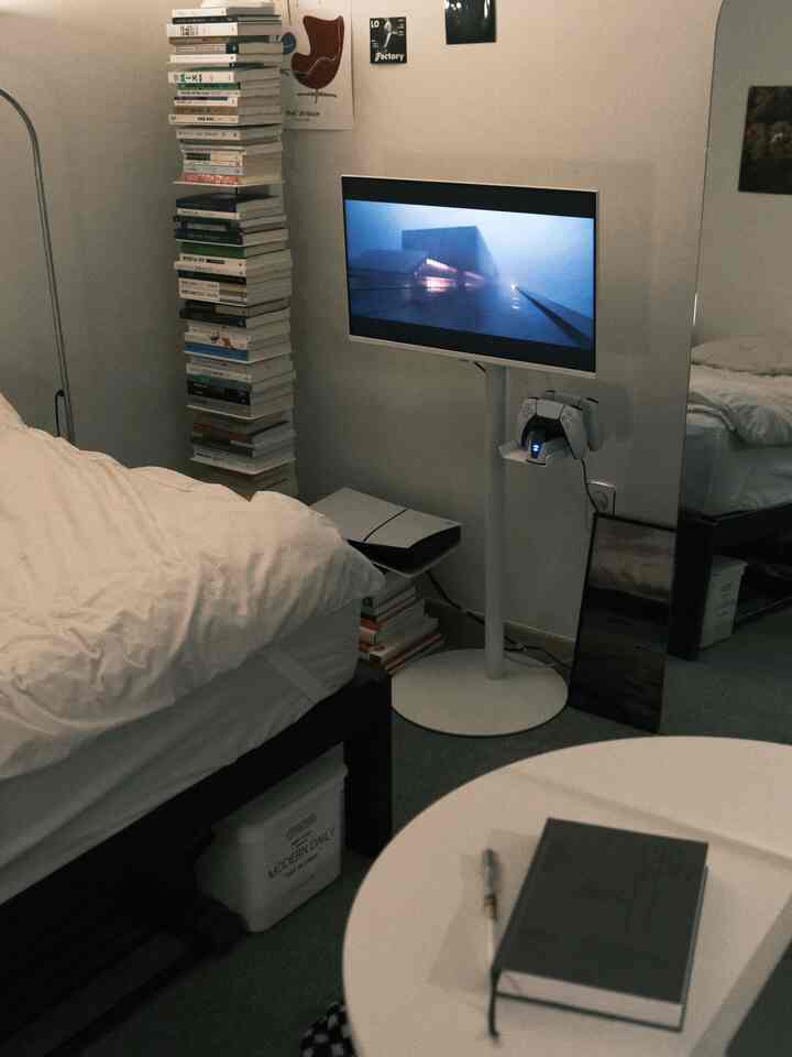 ホワイトとブラックのワンルーム寝室、ベッド、モニター台、本棚が配置されたコンパクトな空間