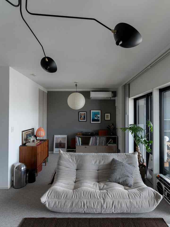 白とグレーの色調のリビング、中央に柔らかい素材のソファと左側に木製のサイドボードが配置されたモダンで自然な雰囲気の空間