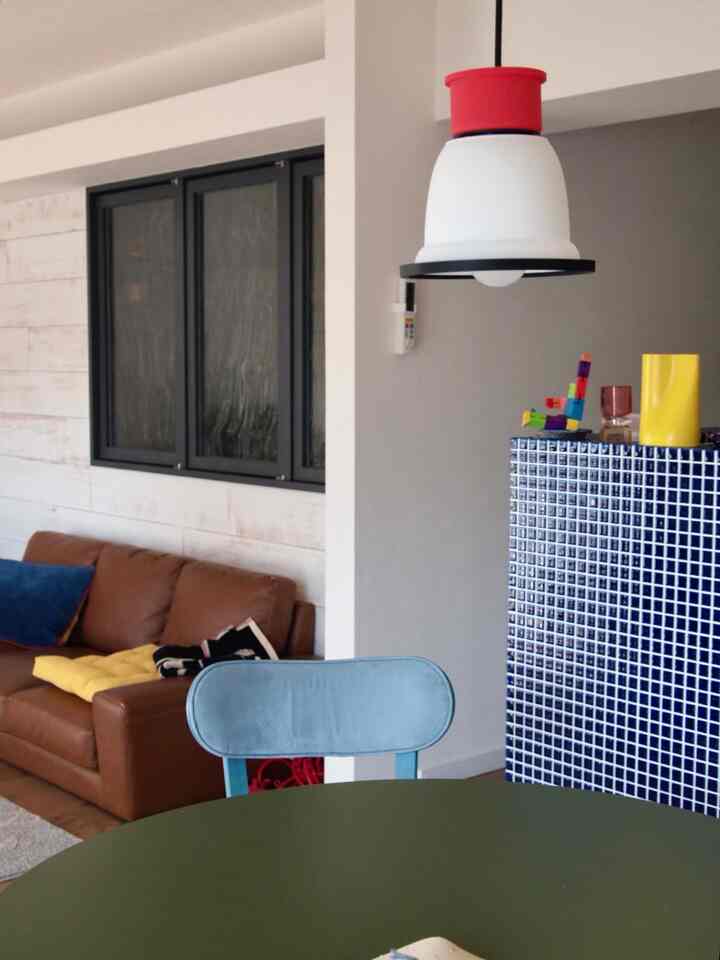 ブラウンのレザーソファと青い椅子が配置されたモダンなリビング、青いタイルのキッチンカウンターと黄色い花瓶が印象的な空間