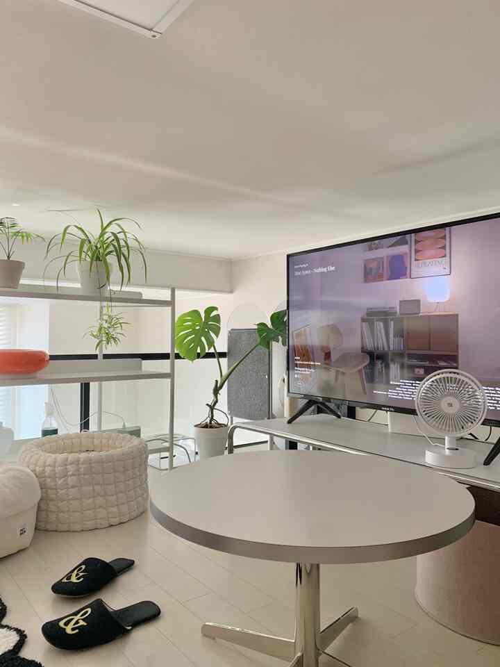 白と緑のトーンが印象的なリビング、丸テーブルとテレビ台、植物が配置されたミニマルでコンパクトな空間