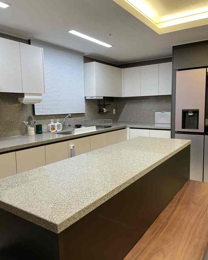 白とグレーのトーンのキッチン、広いキッチンアイランドとモダンな収納が配置された清潔感のあるインテリア