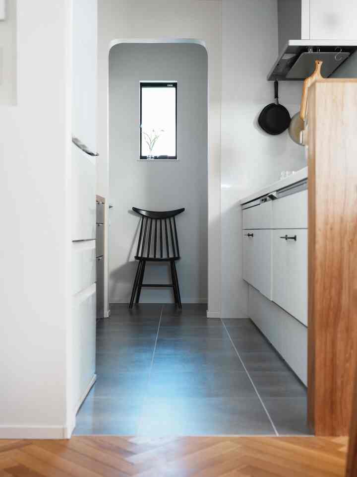 Nordic kitchen pantry featuring a black chair, gray tile floor, and herringbone wood flooring with natural light creating a serene atmosphere