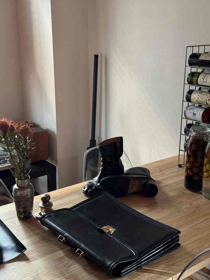 ナチュラルな木目調のダイニングテーブルに黒のレザーのブーツと書類が置かれた雰囲気のあるリビング