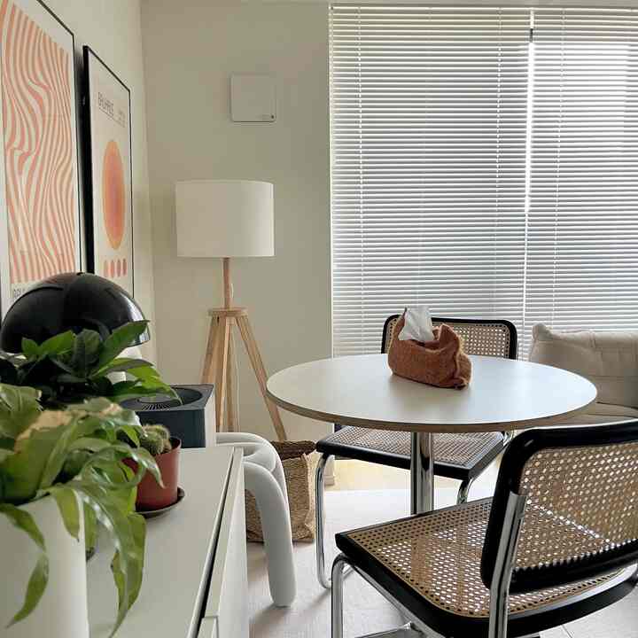 White and natural toned two-person dining space featuring a round dining table, rattan chairs, and a floor lamp with cozy atmosphere