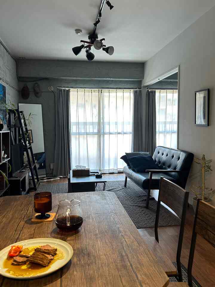 A natural wood tone modern dining room featuring a black leather sofa and wooden dining table, creating a cozy single household atmosphere
