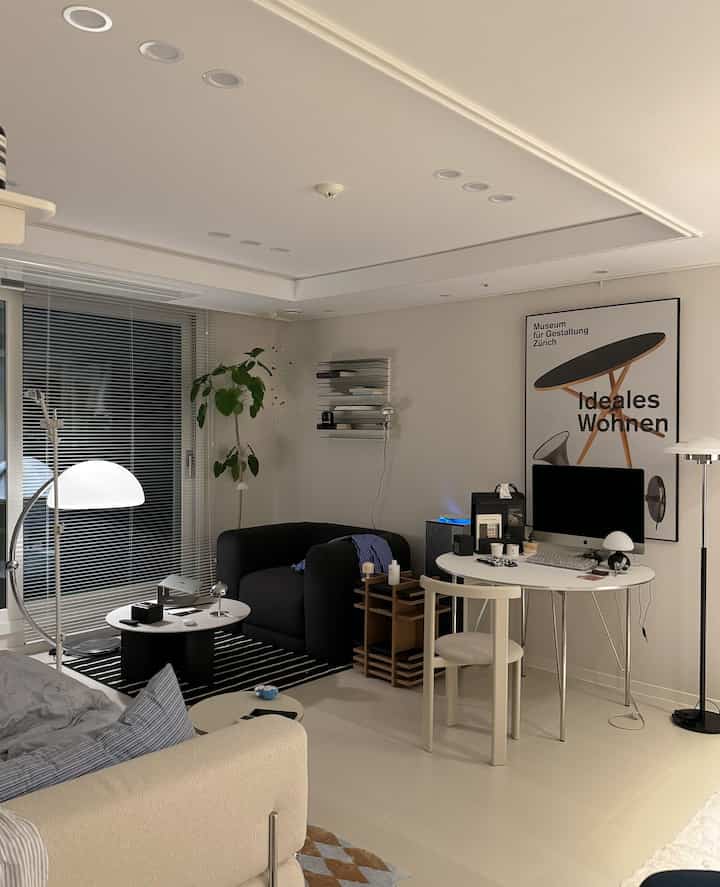 白と黒のトーンのリビング兼ホームオフィス、シンプルモダンな家具と照明が配置された清潔感のあるインテリア