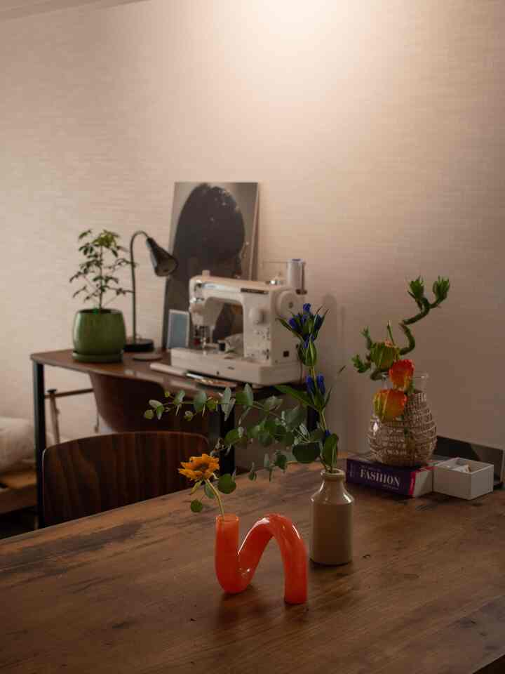 ナチュラルな色調のダイニングルーム、木製のダイニングテーブルと椅子にオレンジ色の花瓶と多様な植物が置かれた雰囲気のある空間