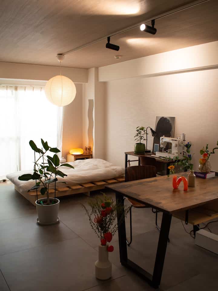 ウッドトーンと白を基調としたワンルーム、ベッドとダイニングテーブル、植物が配置されたナチュラルでミニマルなジャパンディスタイルのインテリア