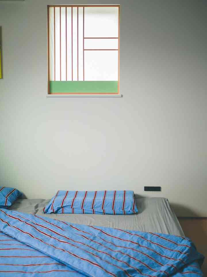 ナチュラルカラーの寝室、モダンな窓枠とエメラルドグリーンのパネル、青いストライプの掛け布団カバーが配置された雰囲気のあるインテリア