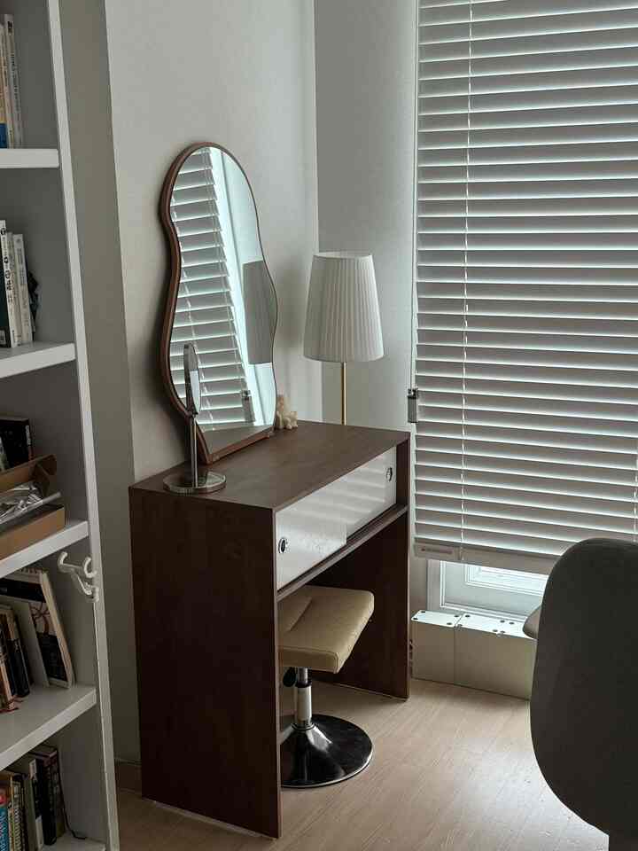 ナチュラルトーンの書斎空間、ダークブラウンのコンソール型化粧台と曲線鏡、白いブラインドとフロアランプが配置された落ち着いた雰囲気のインテリア