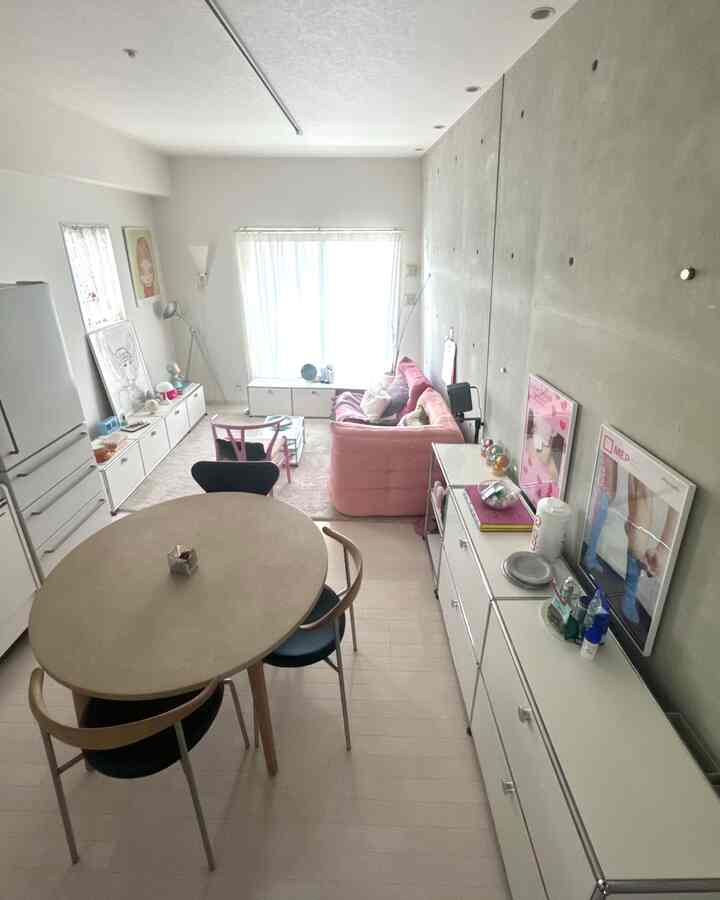 白い壁と自然光の差し込むダイニング兼リビングルーム、ピンクのソファと丸いダイニングテーブルが配置されたモダンで清潔感のあるインテリア