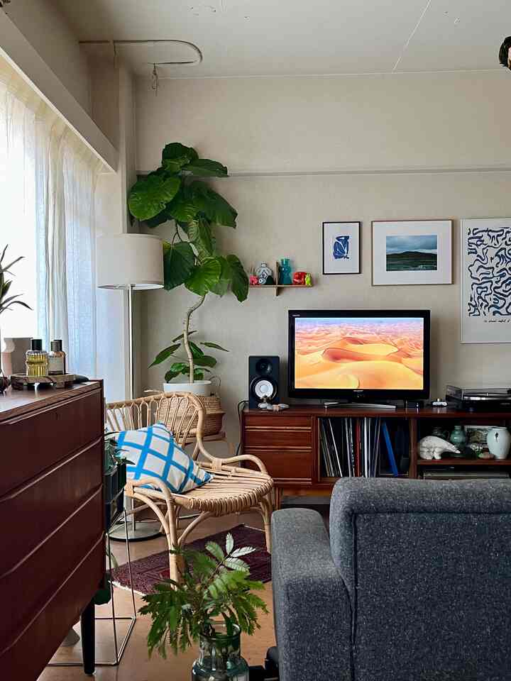 ナチュラルな木目調と緑の植物が調和したヴィンテージ風リビング、ラタンチェアとグレーのソファが配置された雰囲気のある空間