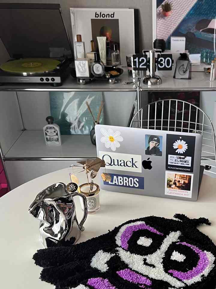 白とグレーのトーンのコンパクトなホームオフィス、滑らかな白いテーブルにアップルのMacBook、ターンテーブル、時計が配置された雰囲気のあるカフェ風インテリア