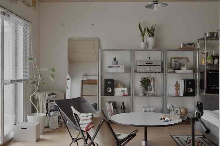 白とブラウンのトーンのリビング、アウトドアチェアと丸テーブル、メタル棚と植物が配置されたモダンな空間