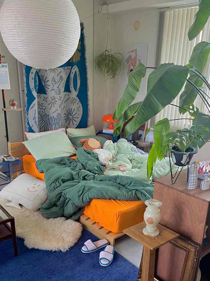 緑とオレンジの色調が印象的な寝室、ベッドと植物が調和した雰囲気のあるインテリア