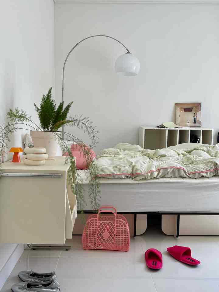 White and pink toned single bedroom featuring plants and simple furniture with cozy and charming accents