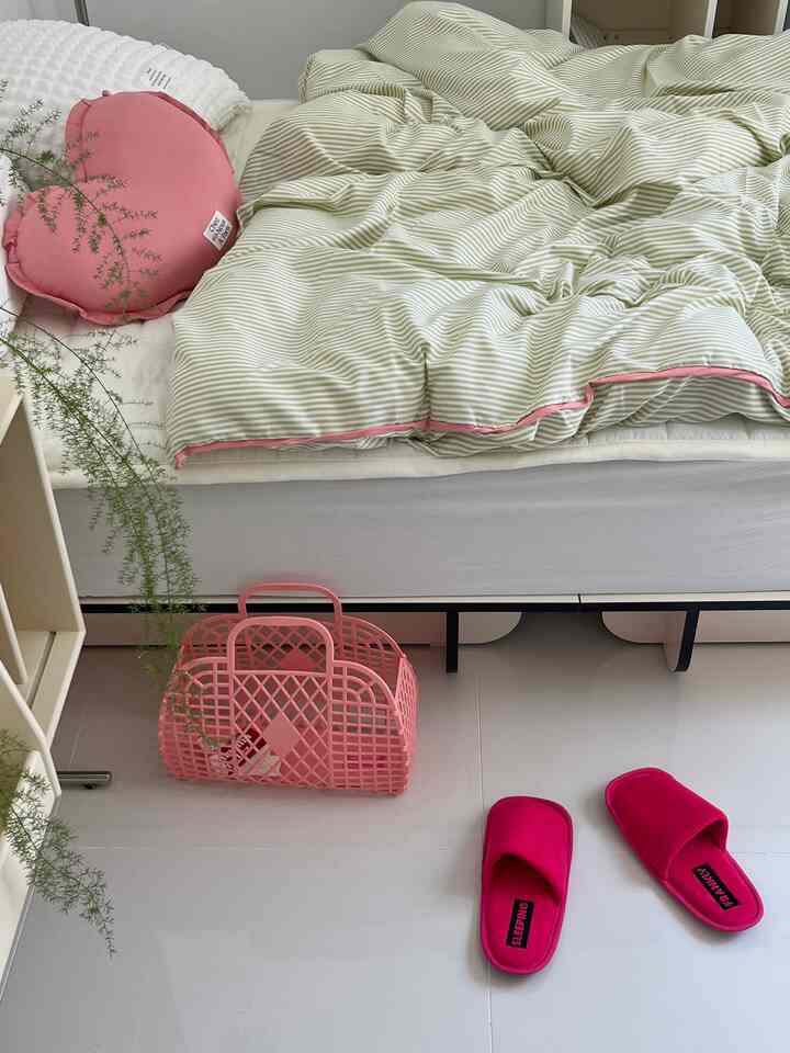 Simple bedroom with white floor and bed, accented by pink cushion and storage basket