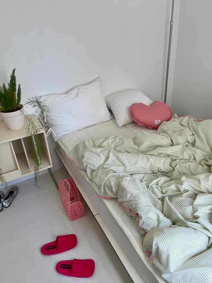 White and beige tone bedroom featuring a tidy bed with cushions and a side table adorned with plants, creating a cozy atmosphere