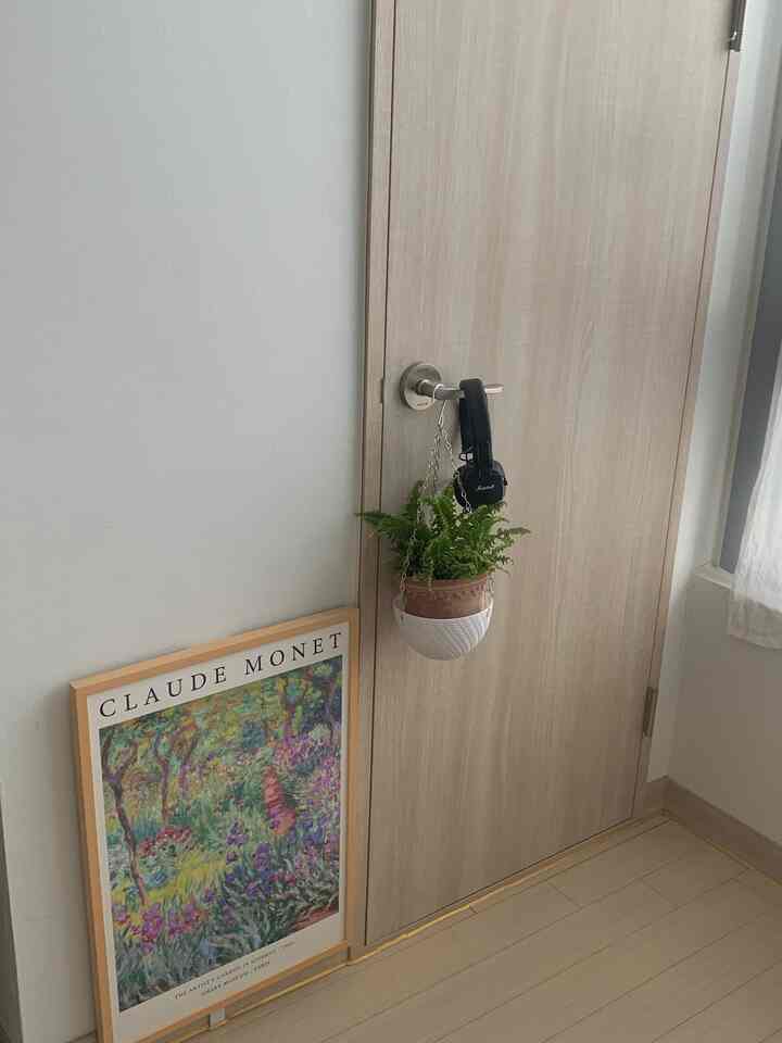 ナチュラルカラーの玄関空間、右側のドアノブに植物が吊るされ、左側の床にクロード・モネのポスターが置かれた雰囲気のあるインテリア