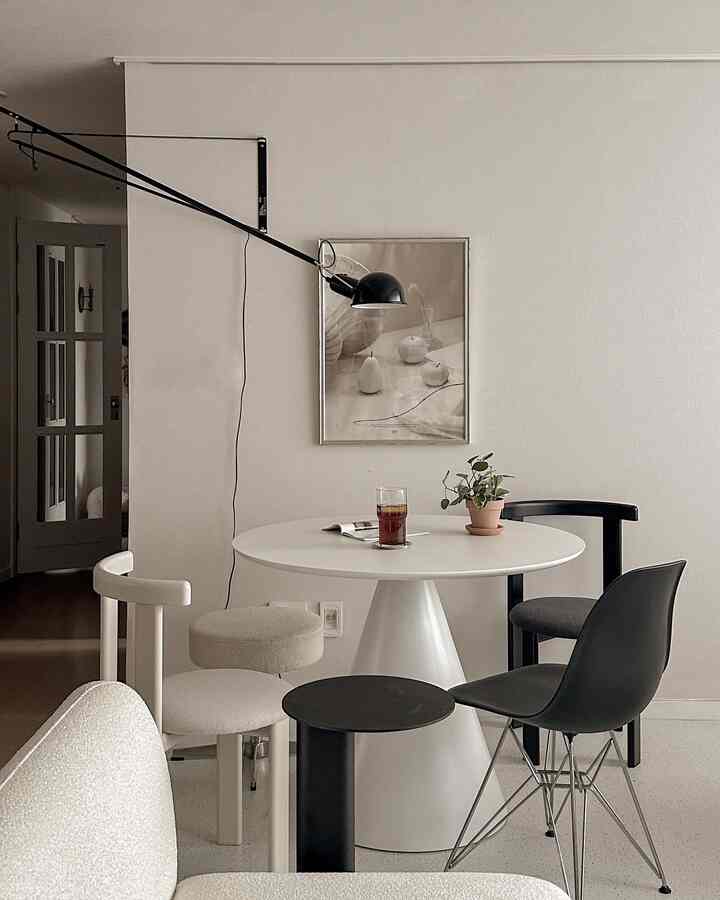 White-toned living room with home cafe setup featuring a round dining table and diverse chairs in a modern cozy space