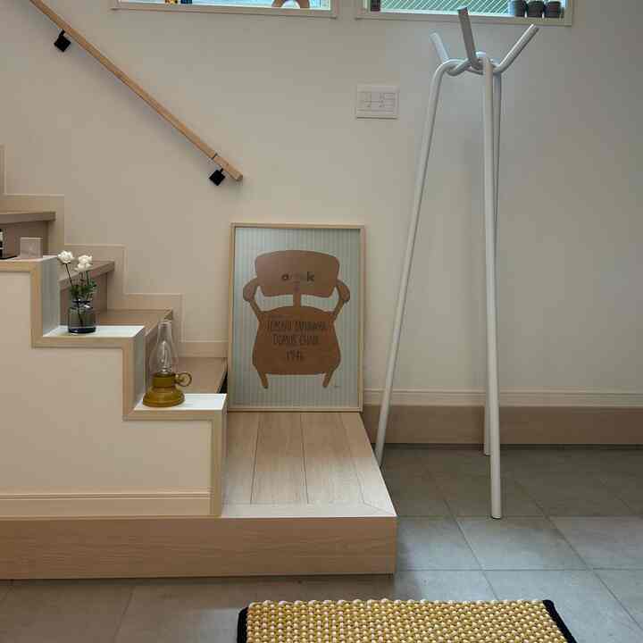 Bright white-walled entrance with wood-toned stairs featuring a poster and coat rack in a simple and natural setting