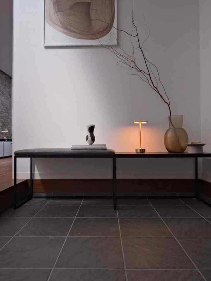 グレーとブラウンの色調の玄関スペース、ベンチとサイドテーブルの上にテーブルランプと装飾的な花瓶が配置された清潔でミニマルなインテリア