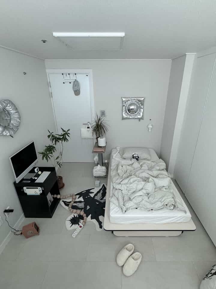 White-tone bedroom featuring a single bed, TV stand, and rug in a simple mid-century modern styled space