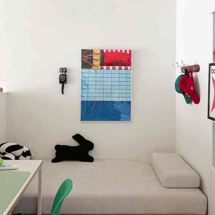 Simple white-toned bedroom featuring a cat-shaped wall clock, framed picture, and a black rabbit cushion on the bed.