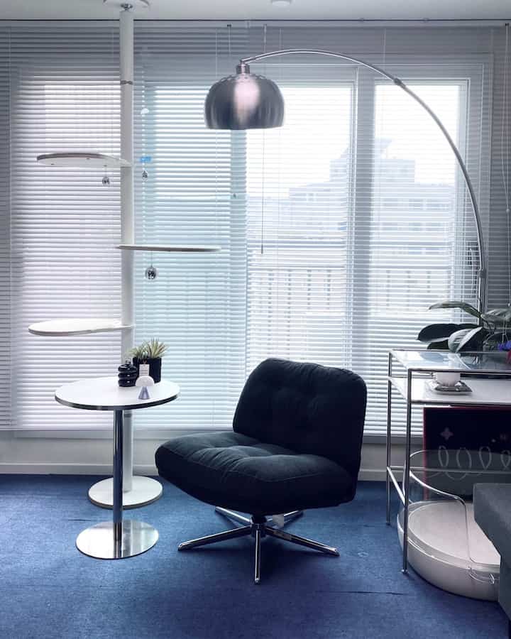 明るいホワイトトーンのリビング、黒のコーデュロイアームチェアと白い丸いサイドテーブル、シルバーのフロアランプが配置されたモダンなインテリア