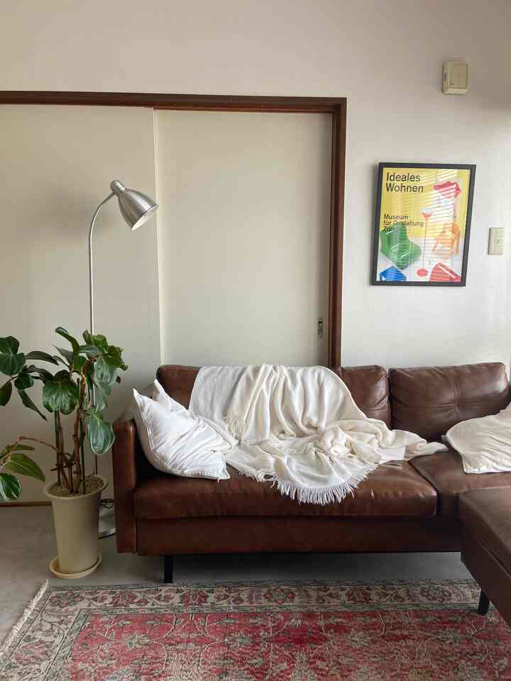 ブラウンのレザーソファと白い壁が調和した、一人暮らし向けのミッドセンチュリーモダンな雰囲気のリビング