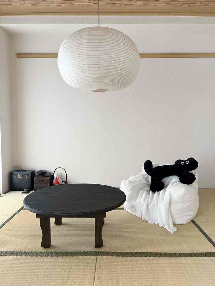 A bright ivory-walled tatami room featuring a black antique round table and white bean bag chair, embodying a simple Wa-Modern style