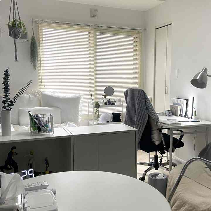 白を基調としたコンパクトなホームオフィス、デスクと透明の椅子、ブラインドが配置されたシンプルなインテリア