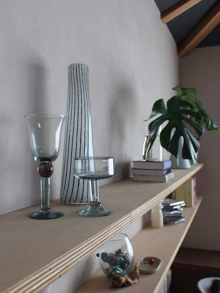 透明なガラス花瓶とモンステラの植物が配置されたナチュラルカラーのリビングの壁棚の印象的なインテリア