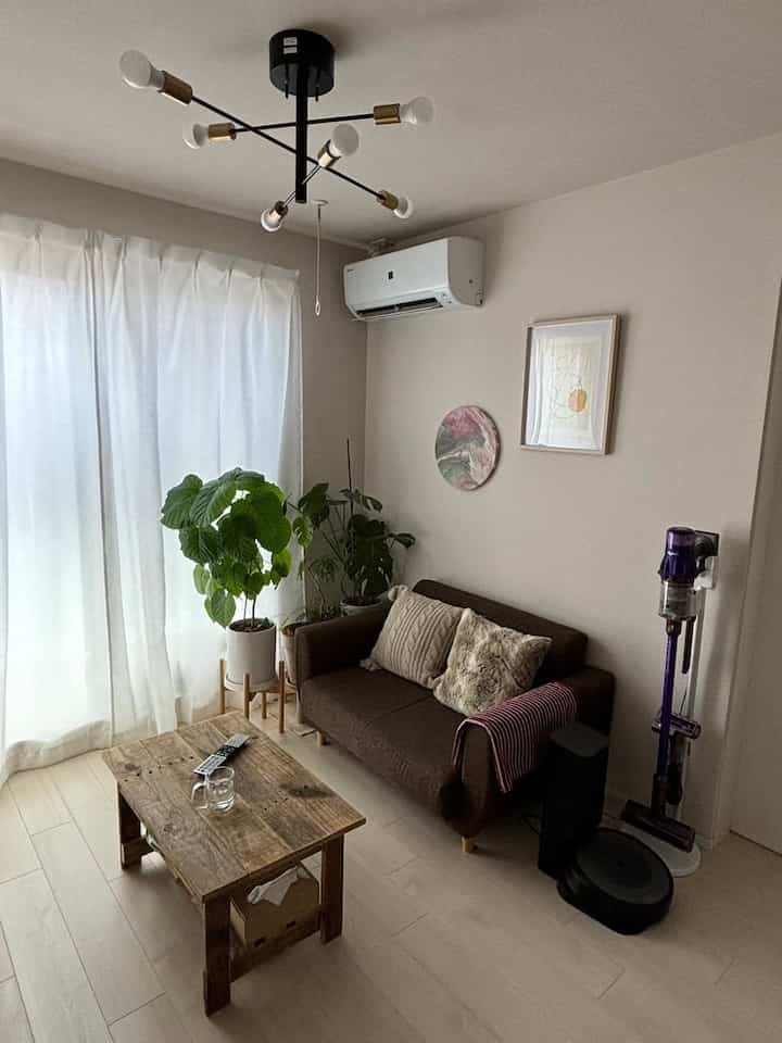 白いカーテンと木目調のテーブルがあるコンパクトなリビング、ブラウンソファと観葉植物が自然な雰囲気を演出