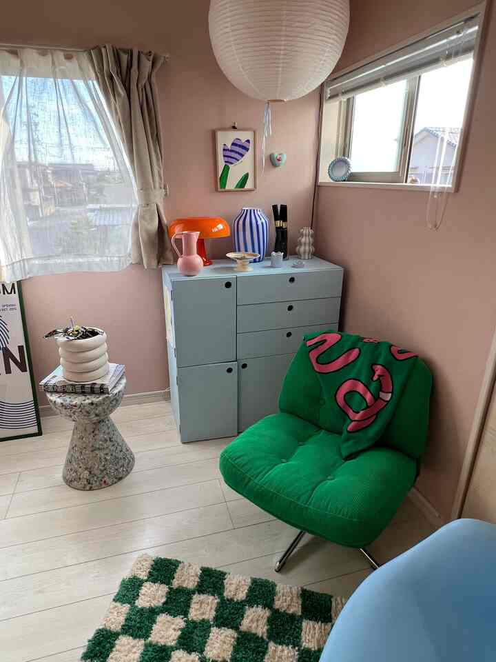 淡いブラウンの床と壁のアールデコ風リビングコーナー、グリーンのアームチェアとパステルブルーの収納家具が配置されたシンプルな雰囲気のあるインテリア