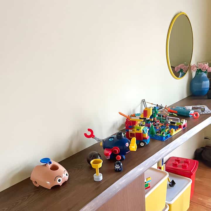 白い壁とブラウンの木製コンソールがある子供部屋、おもちゃと収納ボックスが整えられた印象的な空間