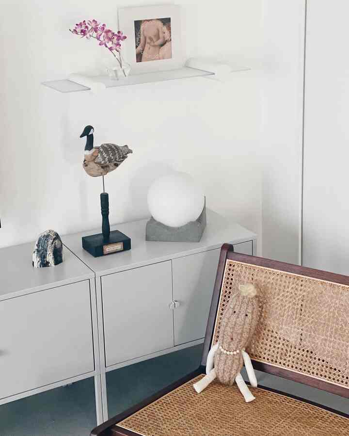 白い壁とキャビネット、ナチュラルな木製ラタンの椅子が配置されたミニマルなインテリア空間