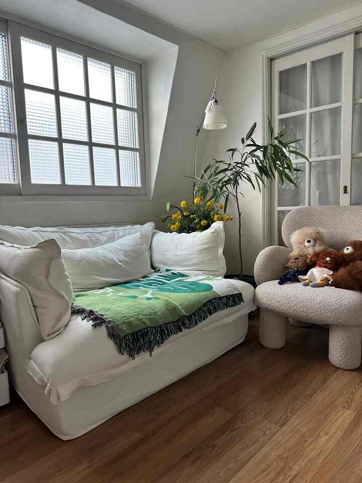 白と緑のトーンのワンルームリビング、ソファとアームチェア、植物が配置された雰囲気のあるインテリア