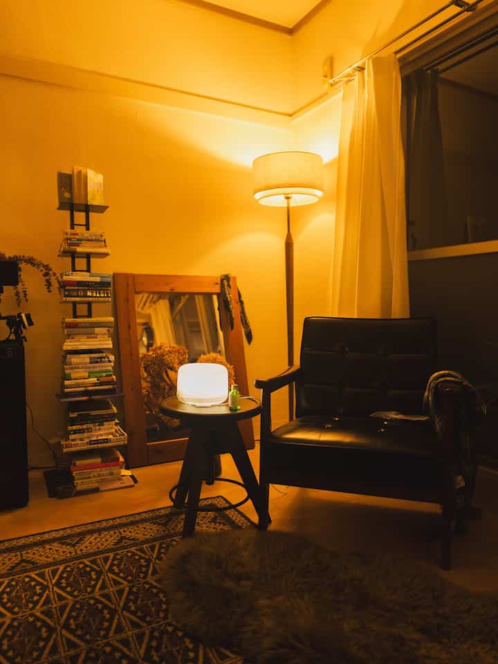 暖かい黄色の照明が灯る小さなリラクゼーションスペース、黒いレザーのアームチェアと木製家具、ディフューザーが調和した雰囲気のあるインテリア