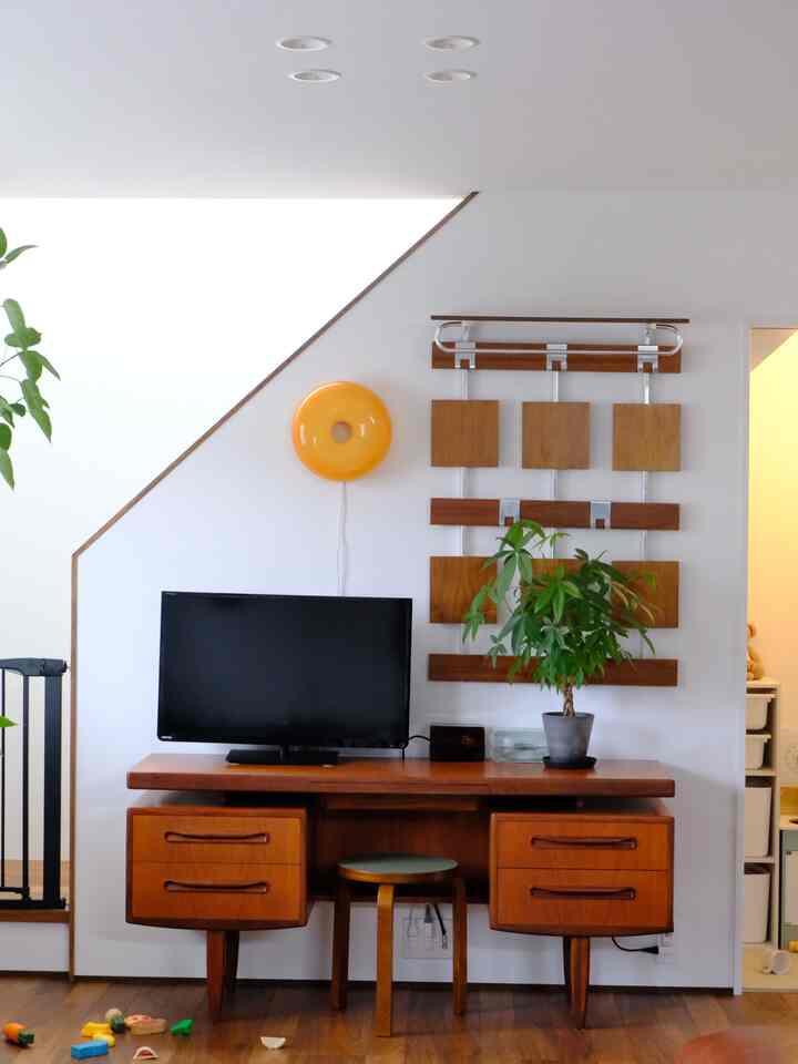 白い壁と木目調の家具が調和したワンルームのホームオフィススペース、スツールと植物が配置されたミニマルなインテリア